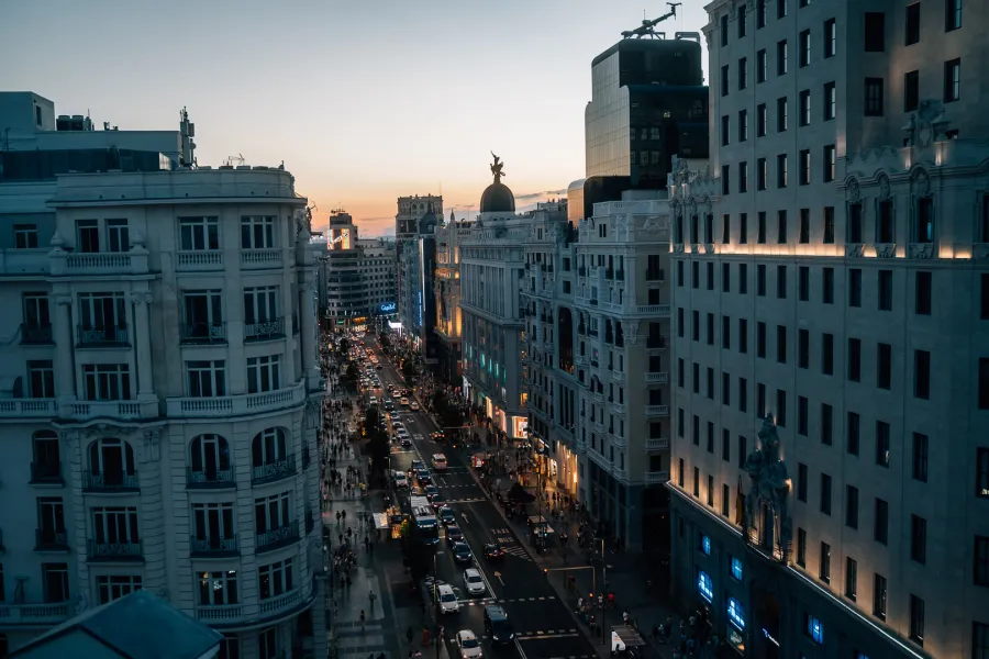 Vista elevada de la concurrida calle Gran Vía de Madrid al atardecer, con coches y peatones en las aceras.