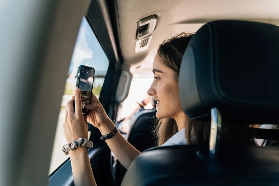 Una joven sentada en el asiento trasero de un coche hace una foto del paisaje con su smartphone.