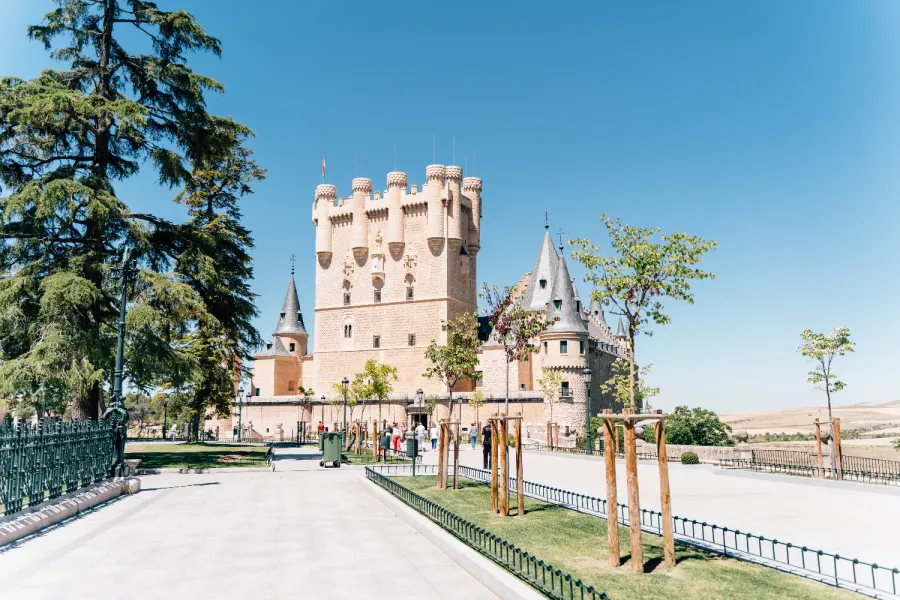 El Alcázar de Segovia, un castillo de piedra con torretas, visto desde un parque en un día soleado.