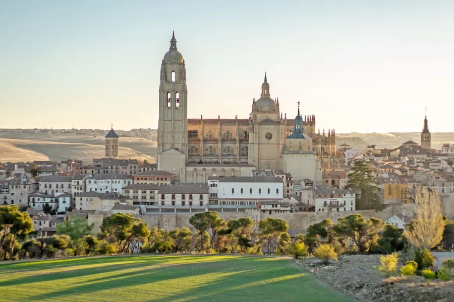 La Catedral de Segovia sobre el casco antiguo, vista desde una colina verde al atardecer.
