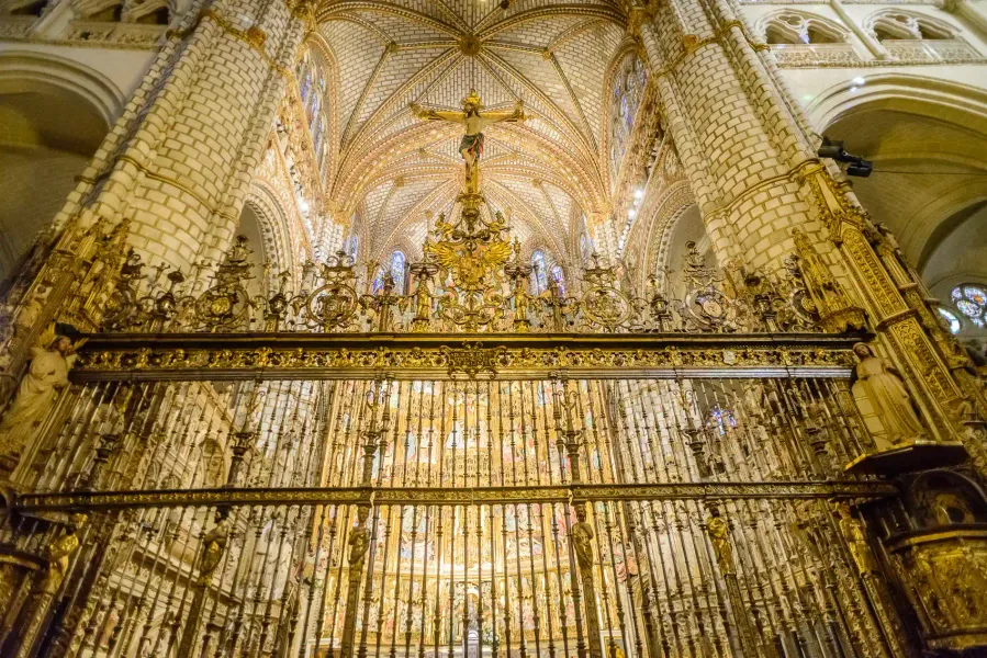 Reja dorada ornamentada bajo un crucifijo y un alto techo abovedado en el interior de la Catedral de Toledo, España.