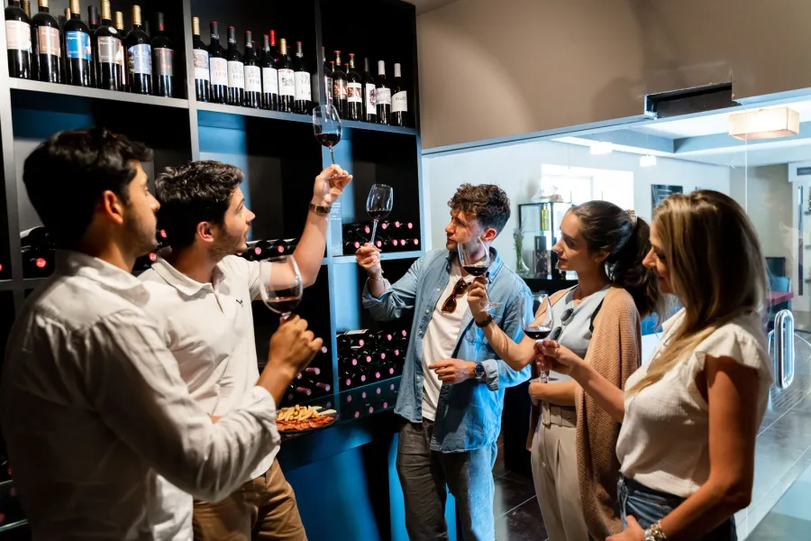 Un grupo de personas catando vino tinto en una tienda. Un hombre levanta su copa para inspeccionar el color del vino.