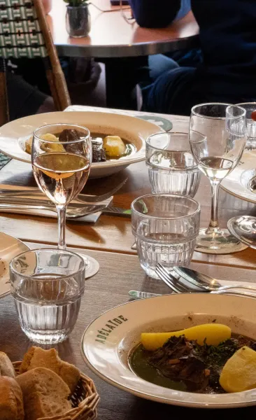 Table set with plates of stew, wine glasses with rosé, and water glasses in a restaurant setting. Focus on food.