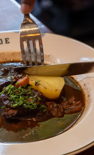 Close-up of a rustic dish, possibly Coq au Vin or beef bourguignon, with a fork. Rich stew, potato, chives.