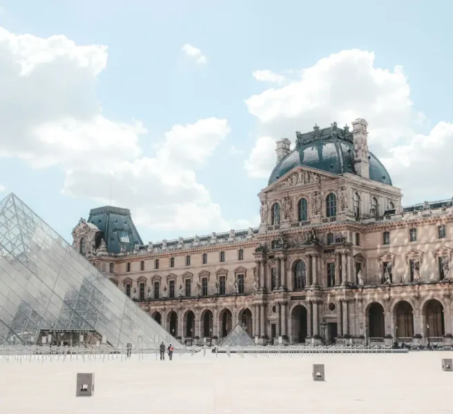 El palacio del Museo del Louvre con una cúpula oscura y la pirámide de cristal en primer plano bajo un cielo nublado.