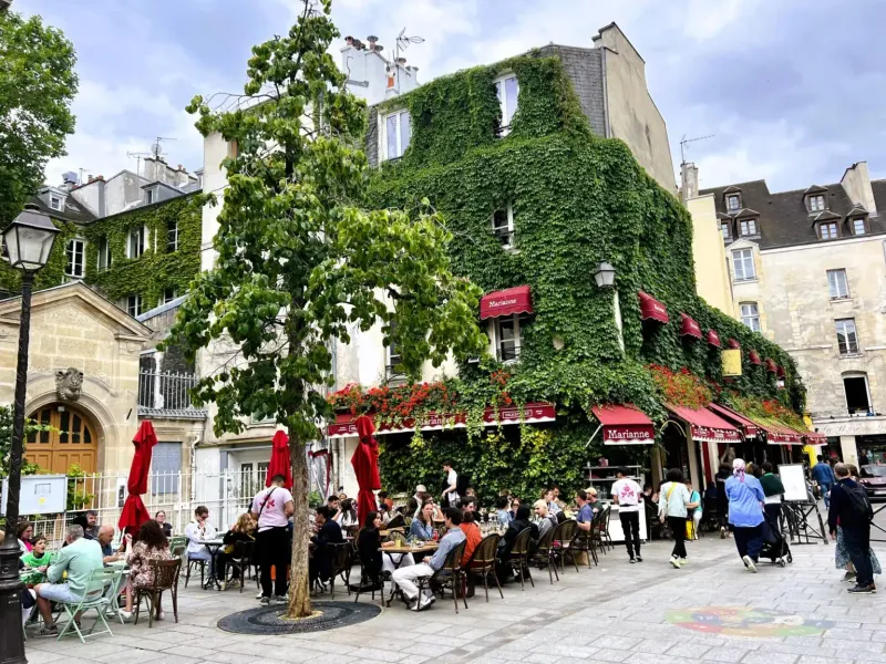 Charming Parisian square with a restaurant named Marianne, surrounded by people enjoying outdoor dining.