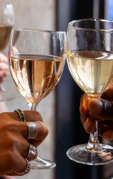 Close-up of three people's hands raising wine glasses with white and rosé wine for a toast.