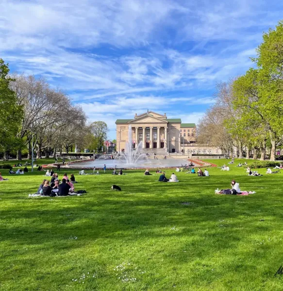 Edificio del Gran Teatro, fuente y gente relajándose en la hierba verde del parque en Poznań en un día soleado.