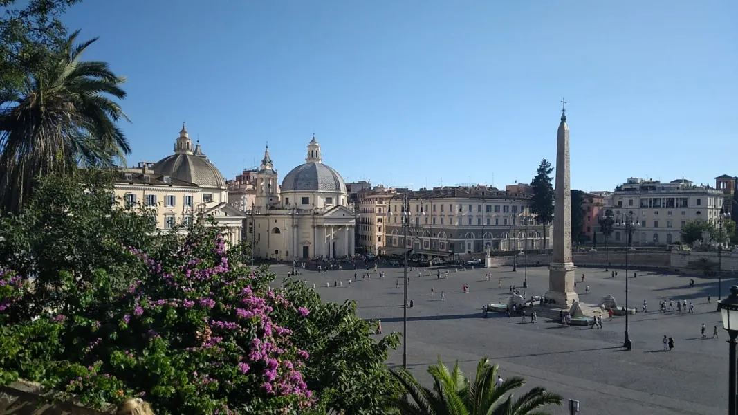Elevated view of Piazza del Popolo in Rome showing the Flaminio Obelisk, twin churches, and people walking in the square.