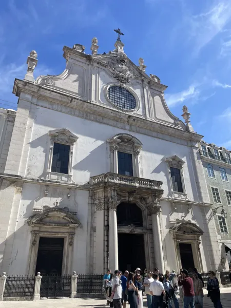Fachada blanca de la iglesia de Sao Domingos en Lisboa con turistas reunidos cerca de la entrada en un dia soleado.