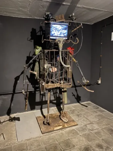 Urzekająca metalowa rzeźba przypominająca robota w klatce, wystawiona w ciemnej galerii.