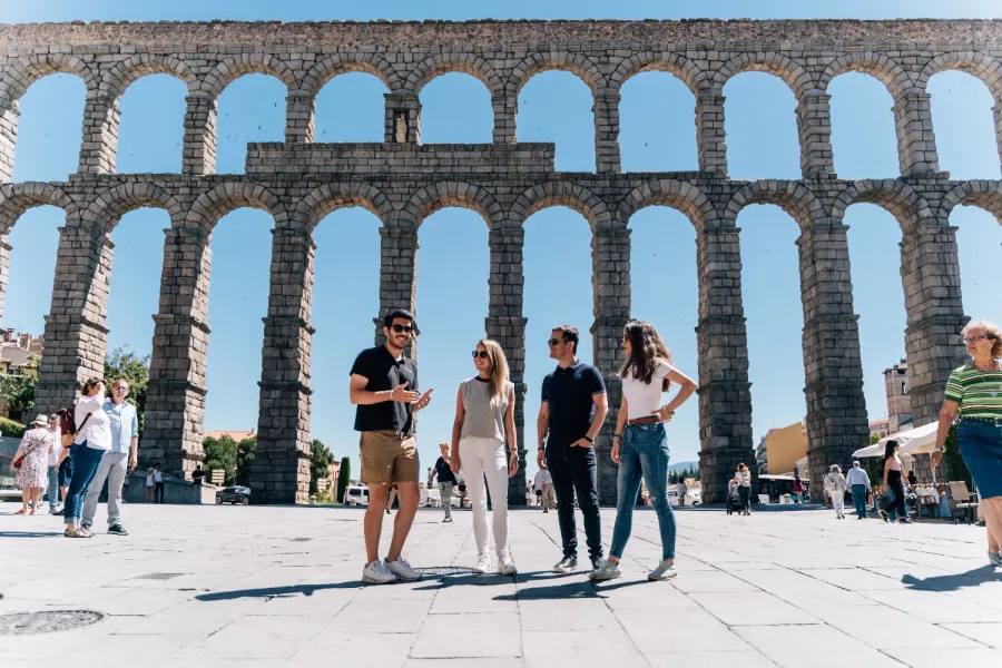 Un guía turístico habla con tres turistas frente al gran y soleado Acueducto de Segovia, España.