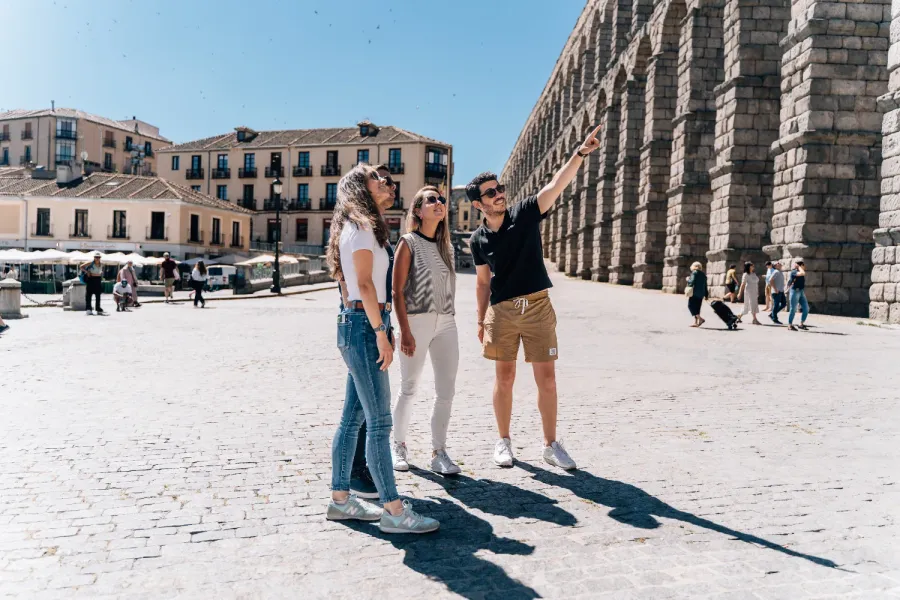 Un guía turístico señala el Acueducto de Segovia a tres turistas en un día soleado.