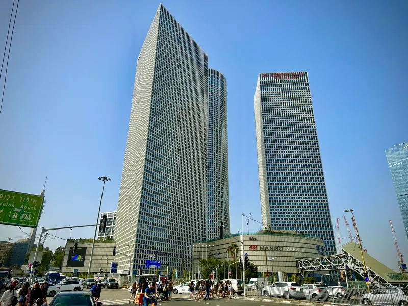 Modern skyscrapers of Azrieli Center dominate the skyline in Tel Aviv, with a busy street, pedestrians, and cars below on ...