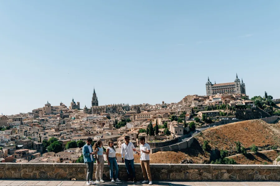Un grupo de personas en un mirador con vistas a la histórica ciudad de Toledo, España, en un día soleado.