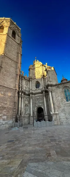 Baroque facade and bell tower of Valencia Cathedral under a clear blue sky, illuminated by sunlight.