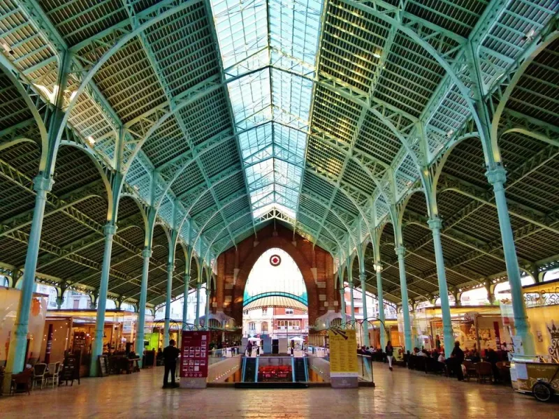 High vaulted ceiling with green metal trusses and a glass roof inside the Colón Market hall in Valencia.