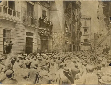 Historic, sepia-toned photo of a crowd gathered on a street in Valencia, in front of the 'El Pueblo' newspaper building.