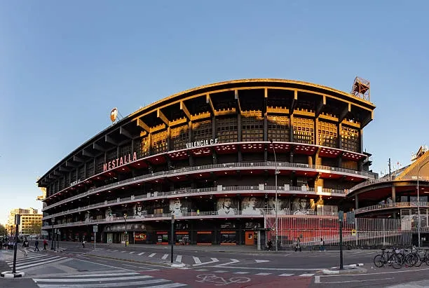 The curved exterior of Mestalla Stadium in Valencia, seen from a street corner during the golden hour.