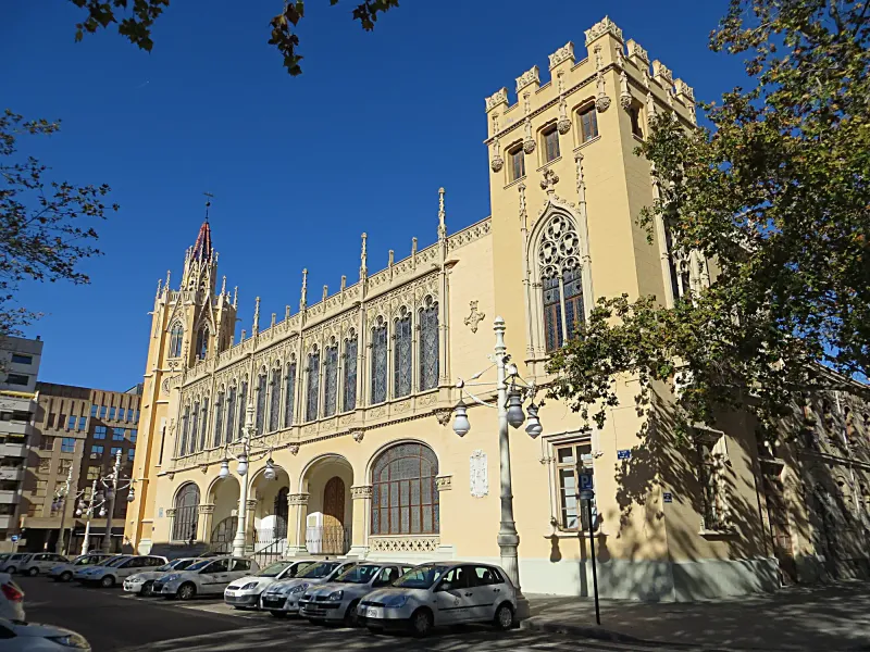 The ornate, neo-Gothic facade of the Palacio de la Exposición in Valencia on a sunny day, with cars parked out front.