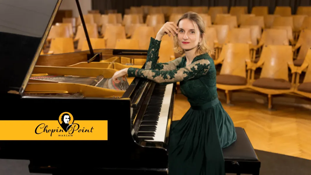 Woman in a green dress sitting at a grand piano in an empty concert hall.