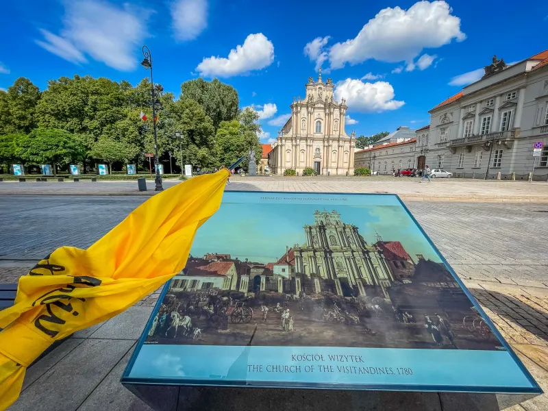 La Iglesia de las Visitandinas en Varsovia, un edificio barroco claro, vista detrás de un panel informativo histórico.
