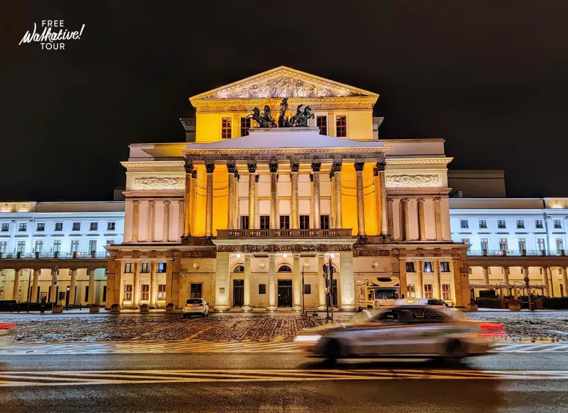 Das Große Theater in Warschau bei Nacht, klassische Fassade mit Säulen und Skulpturen, warm beleuchtet. Schnee auf dem Boden.
