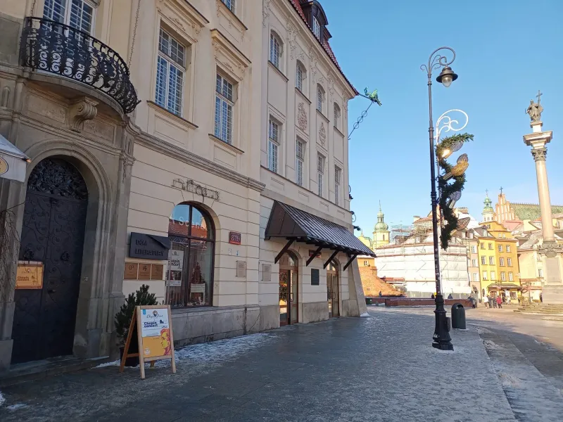 Facade of Dom Literatury (House of Literature) and buildings in Warsaw's Old Town, with a Chopin concert sign. Snowy pavem...