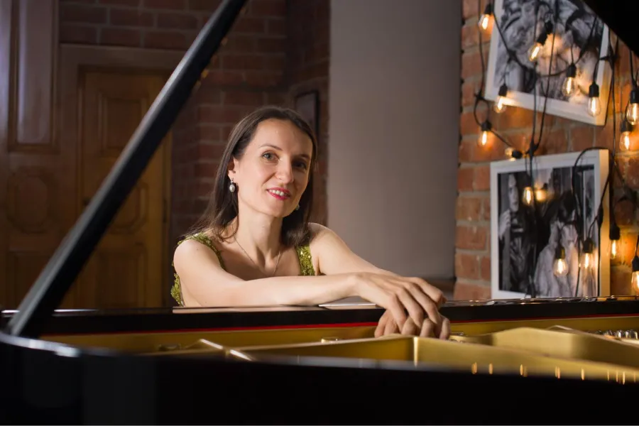 La pianista Aleksandra Hurkała se apoya en un piano de cola en una sala con paredes de ladrillo.