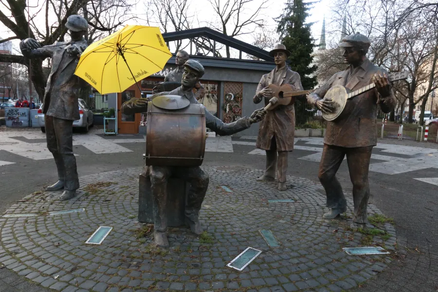 Bronze statue of five street musicians in Warsaw's Praga district, one holding a yellow umbrella, on a cobblestone circle.