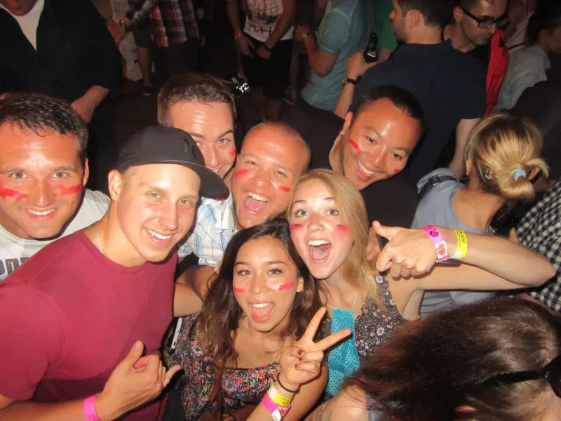 Junge Leute mit roter Gesichtsfarbe auf den Wangen lächeln, posieren eng zusammen bei einem lebhaften Event. Armbänder sic...