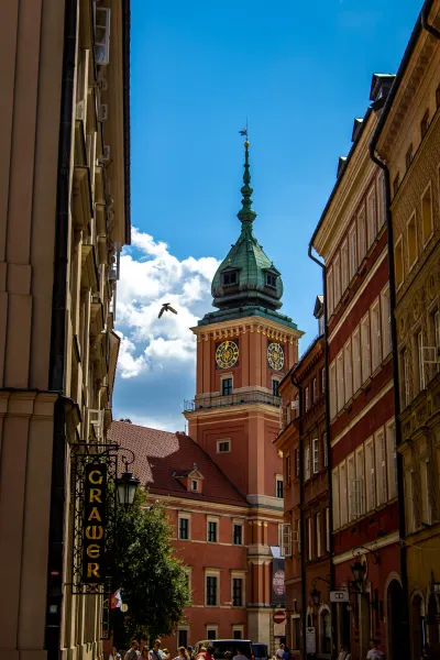 Vista de una calle estrecha hacia la torre del reloj del Castillo Real de Varsovia con cúpula verde, esferas doradas y un ...
