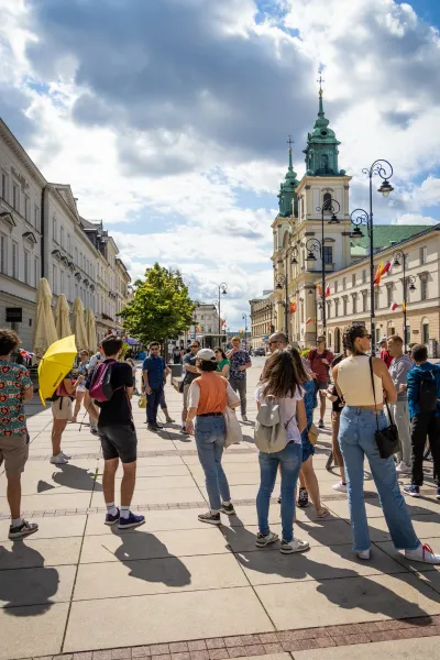 Un grupo de personas reunidas en una calle adoquinada de Varsovia con una iglesia histórica y edificios de fondo bajo un c...