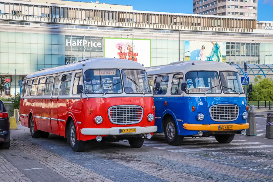 Zwei rote und blaue polnische Oldtimer-Touristenbusse parken auf einer Stadtstraße vor einem modernen Gebäude.