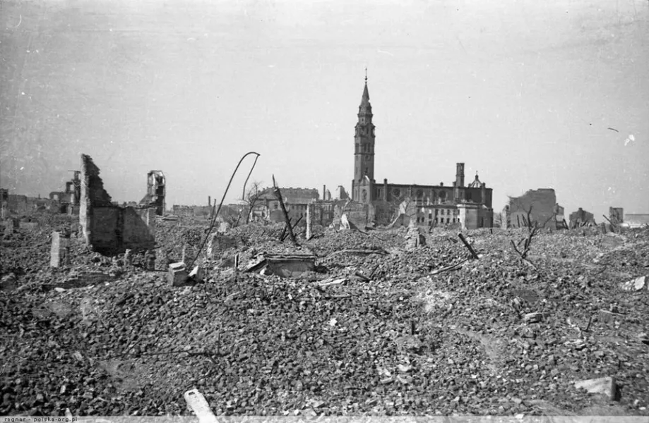 Foto en blanco y negro de una ciudad devastada por la guerra, con un vasto campo de escombros en primer plano y una iglesi...