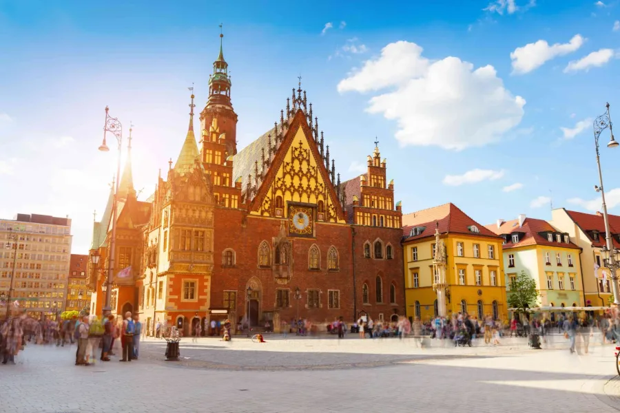 Wroclaw Old Town Hall and colorful surrounding buildings on Market Square, with blurred tourists and bright sunlight.