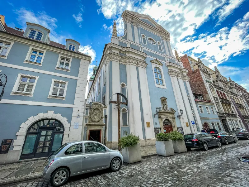 Jasnoniebieska barokowa fasada kościoła św. Antoniego z Padwy przy brukowanej ulicy we Wrocławiu pod błękitnym niebem.