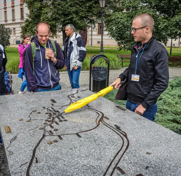 Reiseführer zeigt mit gelbem Regenschirm auf eine taktile Karte von Breslau, während eine Touristengruppe zuhört.