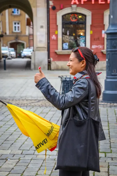 Przewodniczka z żółtym parasolem Walkative daje kciuk w górę na brukowanej ulicy we Wrocławiu.