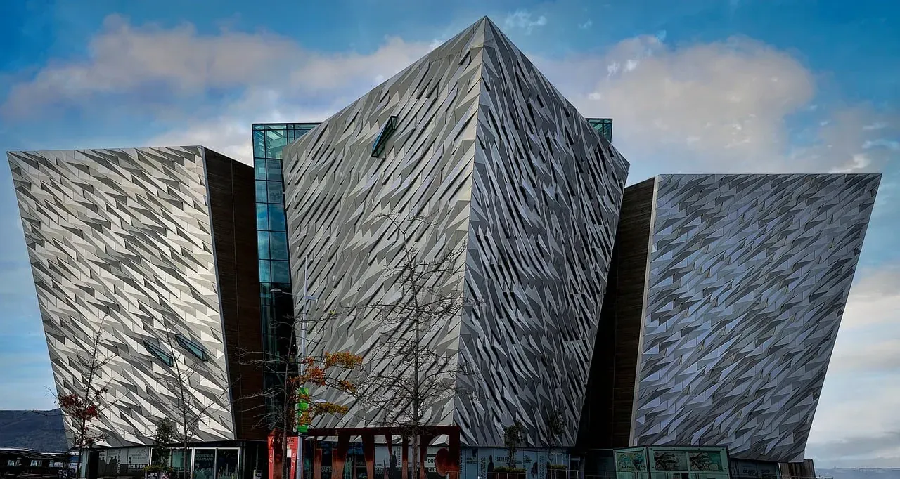 Das Titanic Belfast Gebäude mit seinen kantigen, facettierten Silberpaneelen unter teilweise bewölktem Himmel und kahlen Bäum
