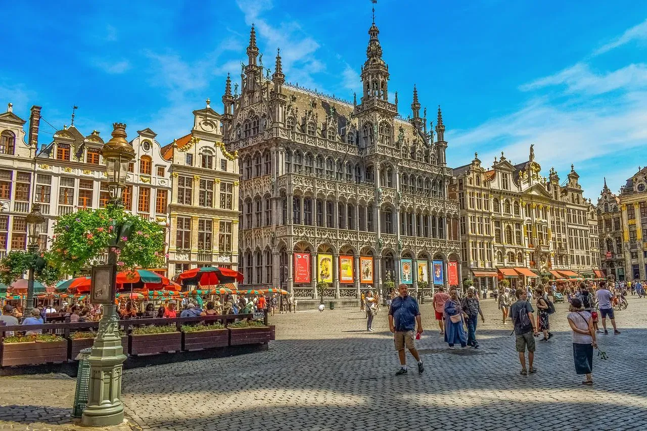 Grand Place in Brussels with ornate historic buildings, outdoor cafes, and people walking on a sunny day.