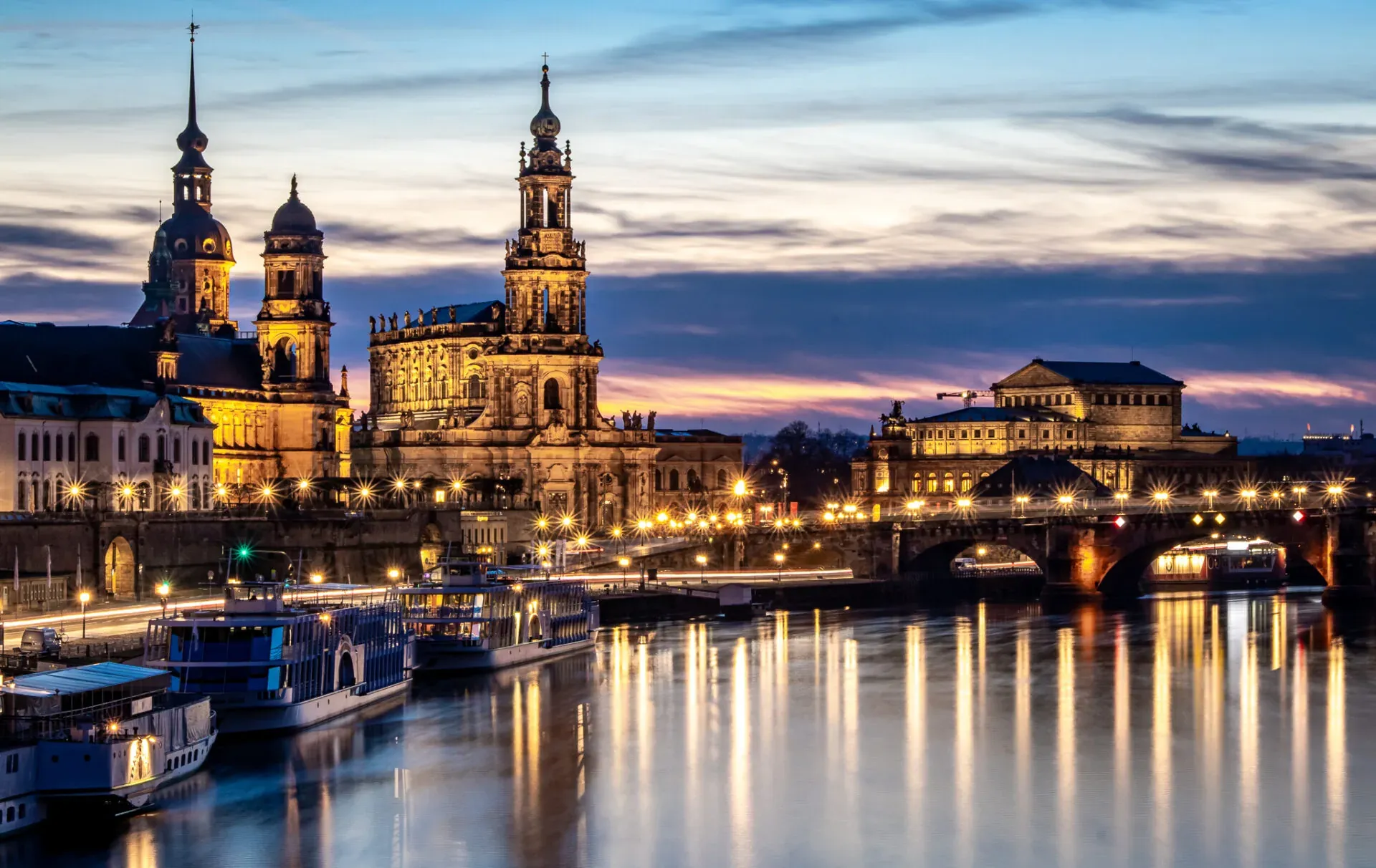 Dresden's Old Town skyline with the Cathedral and Augustus Bridge, illuminated at dusk over the Elbe River.