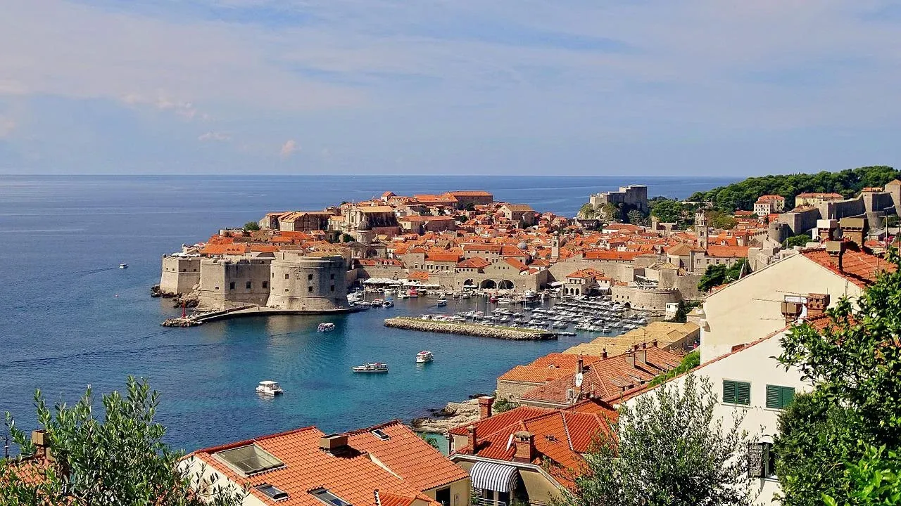Erhöhte Ansicht der Altstadt von Dubrovnik mit roten Ziegeldächern, mittelalterlichen Stadtmauern, Hafen mit Booten und Adria