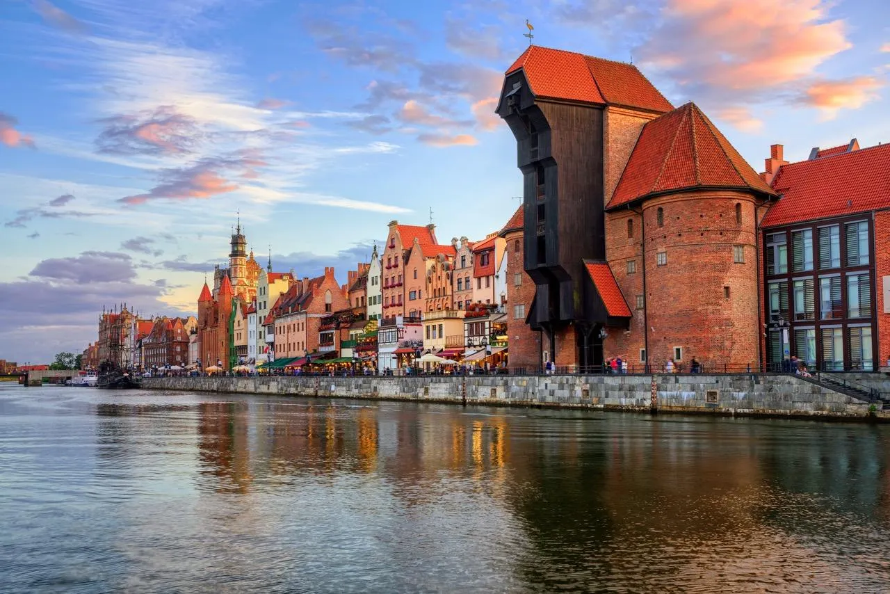 Histórico muelle de Gdansk con la Grúa medieval (Żuraw), casas coloridas y reflejos en el río Motława al atardecer.