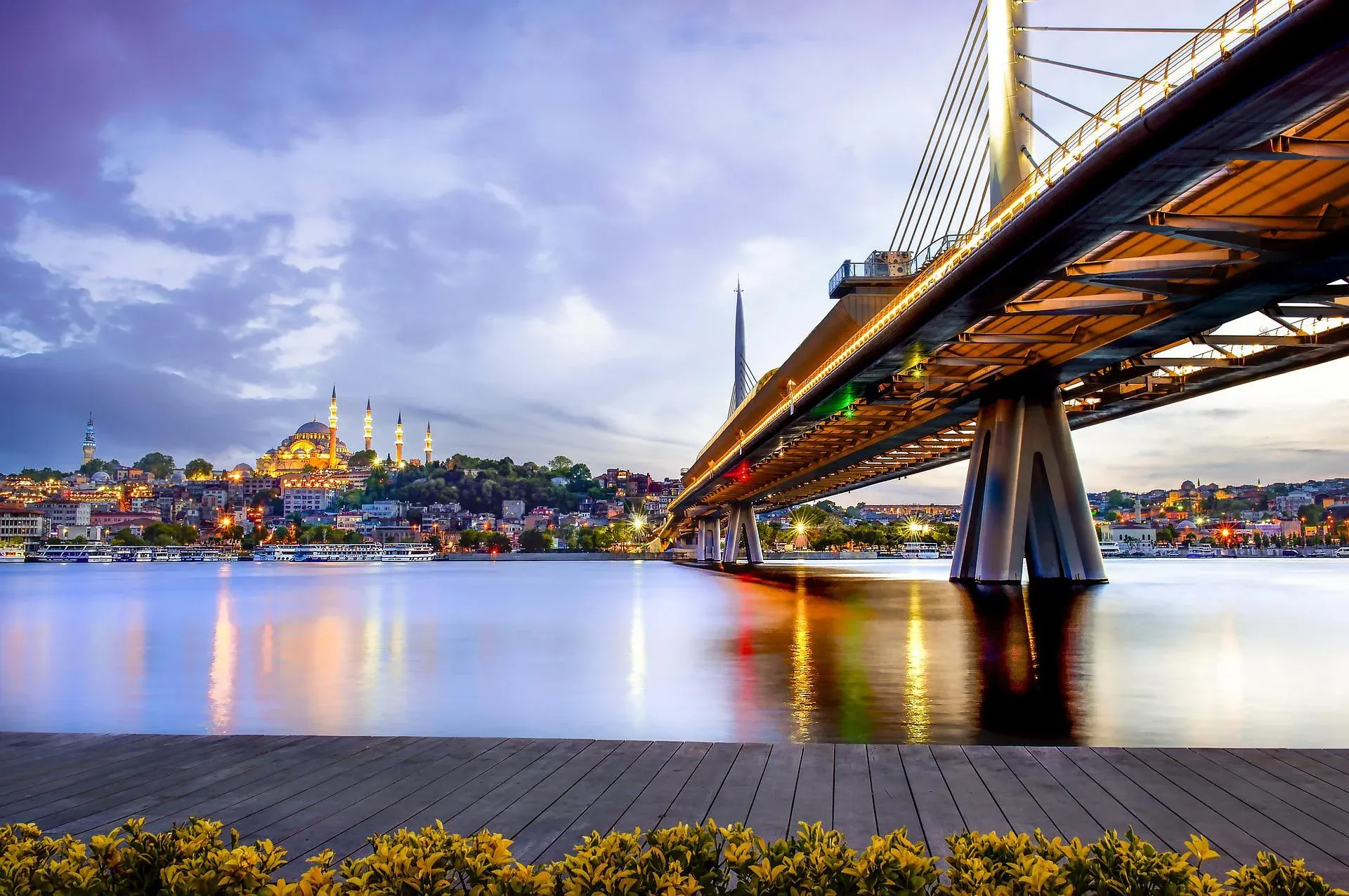 Istanbul's Golden Horn Metro Bridge illuminated at sunset, with the Suleymaniye Mosque visible on the historic skyline.
