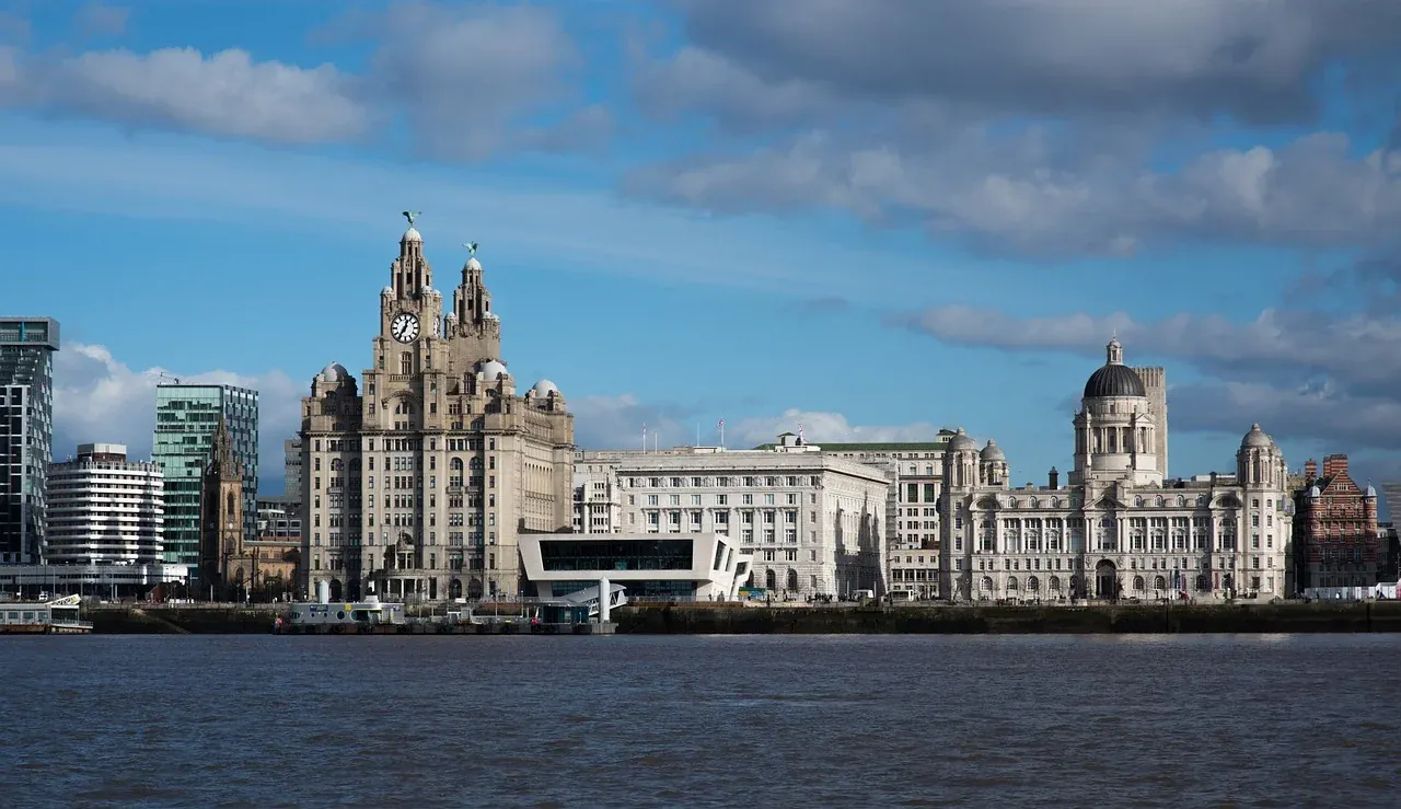 Nabrzeże Liverpoolu z Royal Liver Building, Cunard Building i Port of Liverpool Building pod częściowo zachmurzonym niebem.