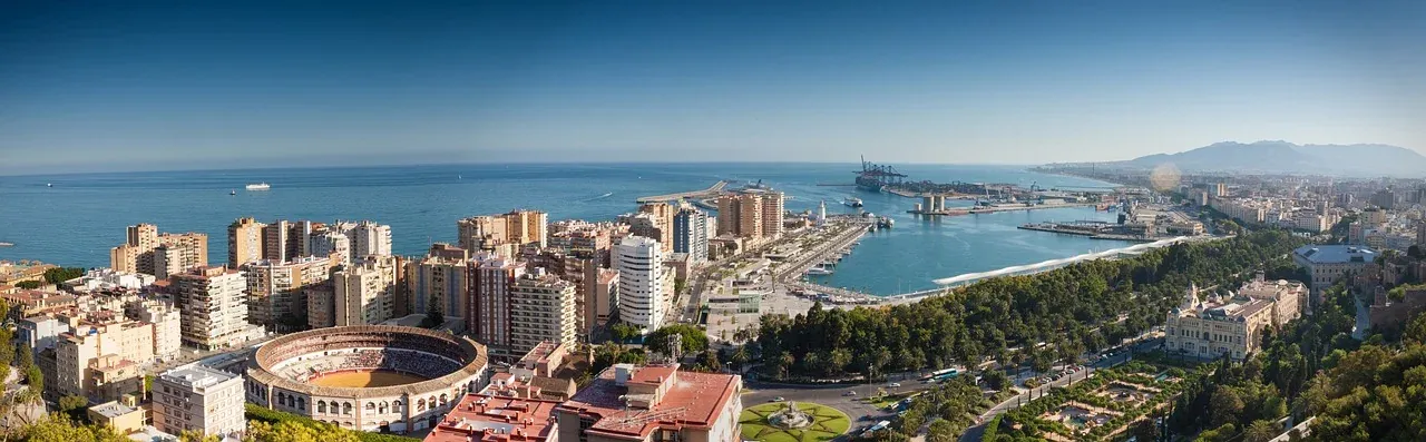 Panoramablick auf Malagas Stadtbild mit der Stierkampfarena La Malagueta, dem Hafen und dem Mittelmeer unter blauem Himmel.