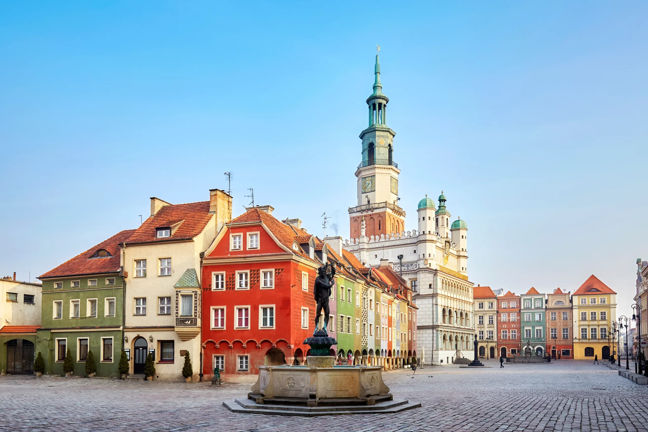 Cobblestone market square with a fountain and Apollo statue, colorful historic buildings, and a large town hall tower under a