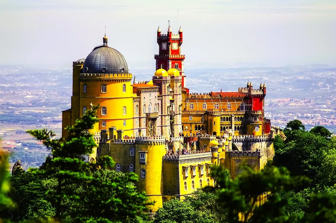 Farbenfroher Pena Palast in Sintra, Portugal, mit gelben, roten und grauen Abschnitten, Kuppeln und Türmen, von Weitem durch