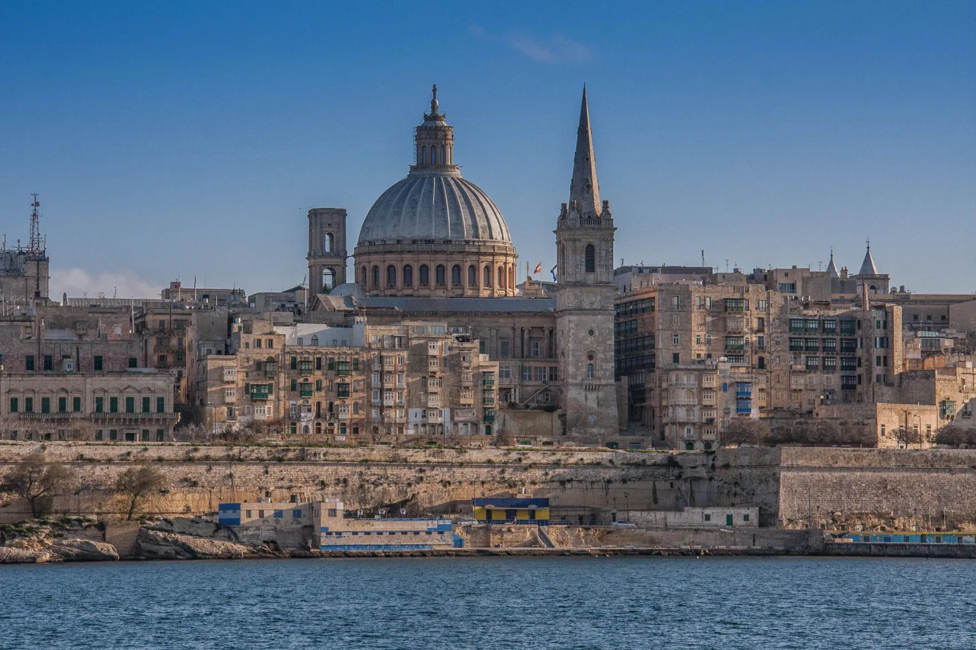 Valletta skyline with Grand Harbour, featuring a large cathedral dome and spire rising above historic buildings.